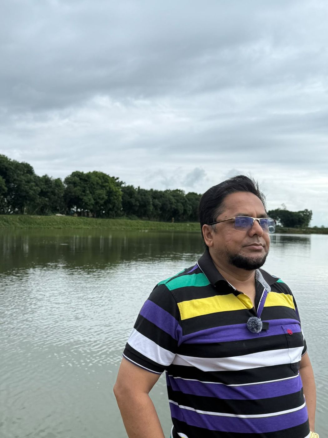মেঘলা আকাশের নিচে শান্ত পুকুর ও সারি সারি গাছ